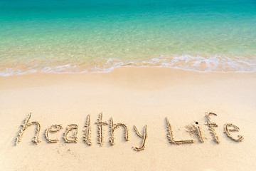 healthy life, lettering on golden sand beach with wave and clear blue sea. message handwritten in sa