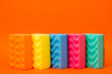 Multicolored sponges for cleaning and washing dishes on a orange background. Space for text