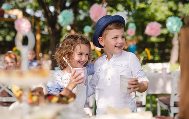 Small children standing outdoors in garden in summer, holding drinks.