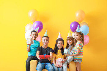 Little children with Birthday gifts and air balloons on color background