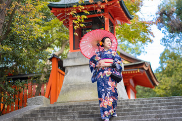 Geishas girl wearing Japanese kimono among red wooden Tori Gate at Fushimi Inari Shrine in Kyoto, Kimono is a Japanese traditional garment. The word 