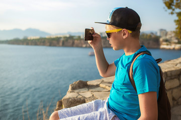 White young kid taking photos of great sunny beautiful landscapes using digital camera of mobile smartphone. Horizontal color photography.