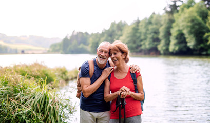 Senior tourist couple on a walk in nature, standing by lake.