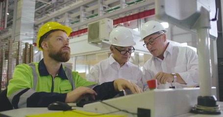 Team of industrial engineers and workman discuss data on display of working CNC machine on background of factory. Equipment debugging and checkout made by technicians