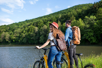 Wall Mural - young tourist couple with electric scooters in nature, standing by lake.