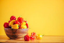 Colorful Scotch Bonnet Chili Peppers In Wooden Bowl Over Orange Background. Copy Space.