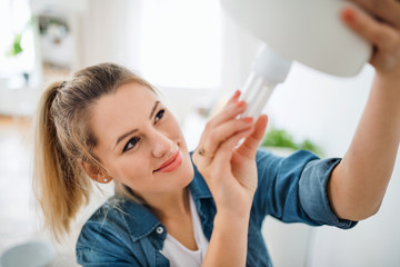 Wall Mural - Young woman indoors at home, changing light bulb.