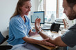 © Maskot - Smiling doctor examining male patient's hand while sitting in medical examination room at clinic