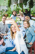 © Maskot - Woman taking selfie with family and friends at dining table in garden party