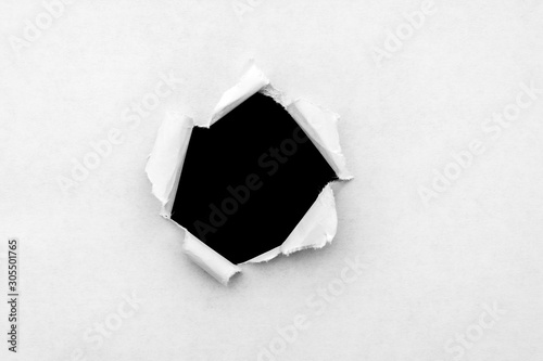 Fotografía A round hole in white paper with torn edges and a black isolated background inside