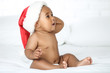 American baby girl in santa hat sitting on white bed