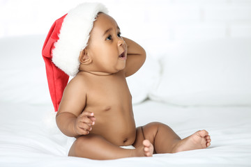 Wall Mural - American baby girl in santa hat sitting on white bed