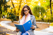 © dianagrytsku - Happy young woman with a notebook in hands sitting on a park bench