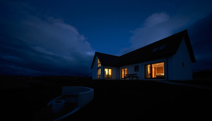 the warm glow of lit rooms from a remote scottish highland croft, bungalow at dusk in winter.