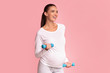 Smiling Pregnant Lady Exercising With Dumbbells Standing On Pink Background