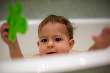 Wall Mural - Cute Caucasian baby gets out of the bath with a green toy in his hand. close-up, soft focus