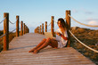 © Macia Puiggros/ADDICTIVE STOCK - Concentrated female freelancer on vacation in white shirt sitting on empty bridge and working with laptop and using mobile phone on blue sky background