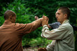 © Mikel Quina/ADDICTIVE STOCK - Bald mature instructor showing exercise to young man in uniform while practicing martial arts on blurred background of forest