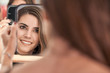 © PHILIPPE DEGROOTE/ADDICTIVE STOCK - Reflection of a beautiful woman face in mirror in hand of smiling lady after cosmetic procedure in salon
