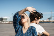© Rafa Cortes/ADDICTIVE STOCK - Attractive pensive woman covering self with hand from sunlight and through fingers while sitting back to back with young man and dreaming against blue sky and blurred modern buildings on square