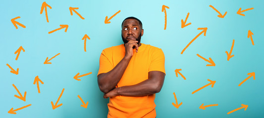 Confuse and pensive expression of a boy with many arrows to follow. cyan colored background