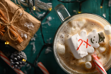 Wall Mural - Christmas composition, mug with hot chocolate with melted snowman marshmallows and caramel. horizontal frame over green background