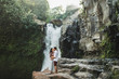 Young couple in love kissing with amazing view of Tegenungan cascade waterfall. Happy together, honeymoon in Bali. Travel lifestyle.