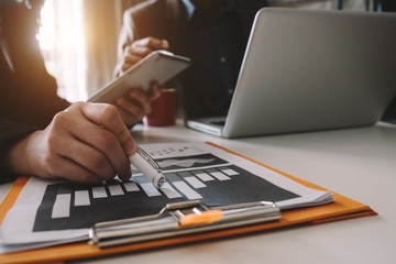 Businessman hand using laptop and tablet with social network diagram and two colleagues discussing data on desk as concept in morning light.