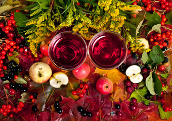 Wall Mural - Mulled wine in a glass cups on a background of fallen autumn leaves with berries, apples and branches of Canada goldenrod (Solidago canadensis). Top view. Autumn background.