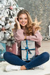 Beautiful girl in pink sweater with christmas box gift near pink and blue Christmas tree. Magical time.