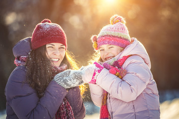 Little girl and her mother playing outdoors at sunny winter day. Active winter holydays concept.