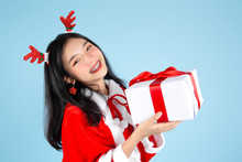 Happy Asian In Santa Claus Costume Holding Christmas  Gift Box On Blue Background.