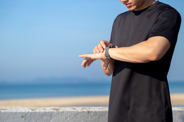 Asian man is setting his smartwatch before go jogging in the morning alongside the sea