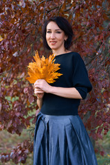 Wall Mural - Beautiful elegant woman standing and posing with bouquet of yellow leaves in autumn city park