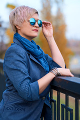 Wall Mural - Beautiful elegant blond woman posing in autumn city park, dressed in blue jeans and jacket