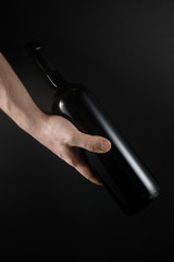 Red wine bottle in the hands of men. Isolated on black exquisite background.