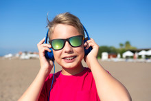 Closeup Portrait Of Cute Sunshine Happy Young Kid Smiling Cheerfully. Teeth With Modern Braces. Boy Wearing Sunglasses And Blue Headphones. Horizontal Color Photography.