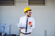 © Dusan Petkovic - Smiling caucasian technologist with helmet on head standing in front of printing shop, holding smart phone and notebook and looking away.
