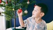 Asian boy is playing with red ball, bauble which decorated on christmas tree 