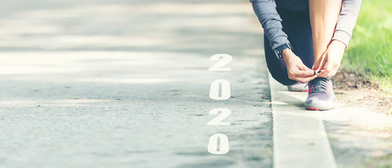 The start into the new year 2020. Start up of runner woman running on nature race track go to Goal of Success.  People running as part of Number 2020.  Holiday sport Concept