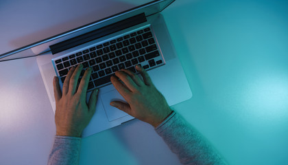 Aufkleber - Man working night online silver laptop in the color light on a table night background. Top view.