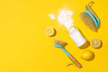 Baking soda, lemon, mustard powder and bamboo brushes against household chemicals products over yellow background. Top view. Copy space. Flat lay. Effective and safe house cleaning