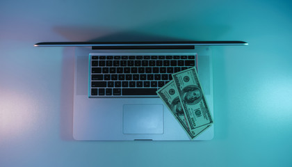 Poster - Beautiful silver laptop and cash dollars banknote in the color light on a table and  background. Work night concept. Top view.