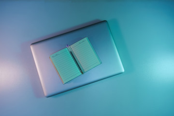 Aufkleber - Beautiful silver laptop and notebook, pen in the color light on a table and night background. Top view.