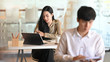 © Prathankarnpap - Young professional female designer working on her project while tablet with co-worker in the background.