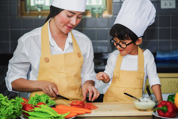 Wall Mural -  Asian woman young mother with son boy cooking salad mom sliced vegetables food son tasting salad dressing vegetable carrots and tomatoes bell peppers happy family cook food lifestyle kitchen