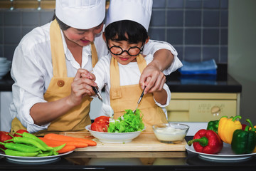 Wall Mural -  Asian woman young mother with son boy cooking salad mom sliced vegetables food son tasting salad dressing vegetable carrots and tomatoes bell peppers happy family cook food lifestyle kitchen