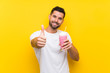 © luismolinero - Young man with strawberry milkshake over isolated yellow background with thumbs up because something good has happened