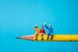 Miniature people, man and woman sitting on yellow pencil using as business and social concept