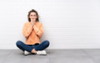 © luismolinero - Young woman with curly hair sitting on the floor with surprise facial expression